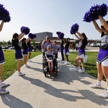 Student in wheelchair entering stadium with cheerleaders cheering him on